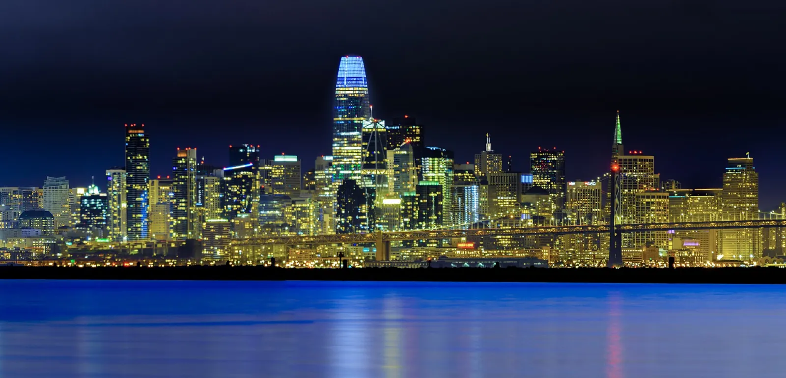 The San Francisco skyline at night, reflected across the bay